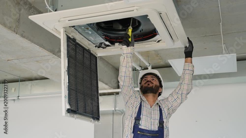 Technician repairing ceiling air conditioner with screwdriver