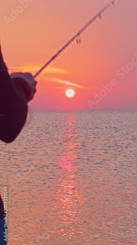 Vertical video. Fishing Rod Pointing Toward Setting Sun Over Sea Horizon Close Perspective Warm Light Reflection Outdoor Angling Scene
