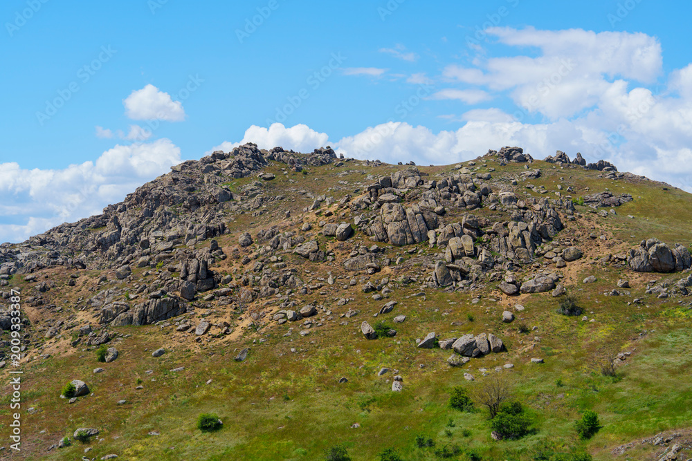 Fototapeta premium Rocky terrain on a hillside with blue sky and clouds during the daytime near a natural location