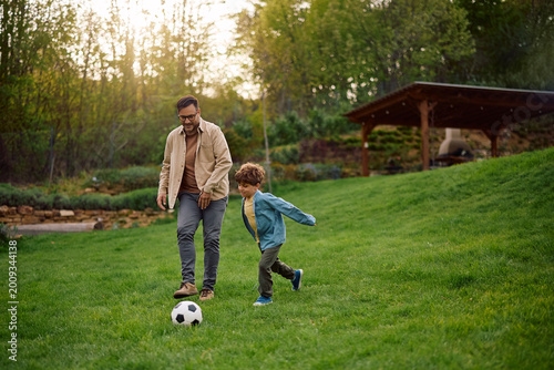 Happy boy and his father playing soccer at park.
