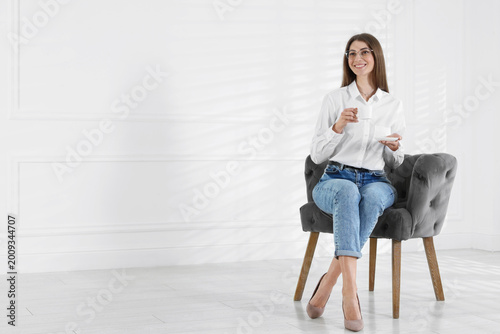 Bild auf Leinwand Happy woman with cup of drink in armchair indoors, space for text