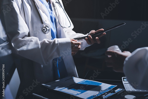 Two doctors and a female nurse meet at a table in the hospital, collaborating on medical tasks using laptops and computers