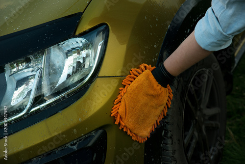Man holds the microfiber gloves in hand and washes the car headlight with detergent. Car detailing. Selective focus