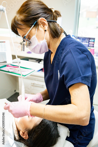 Vertical portrait of a dentist wearing binoculars while cleaning a patient's teeth.