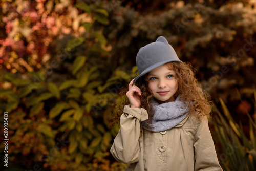 Little cute smiling girl in funny cat hat with long curly hair. Autumn seasonal portrait of young girl outdoor in the garden. Kid fall portrait. Child in the autumn garden. Selective focus, close up