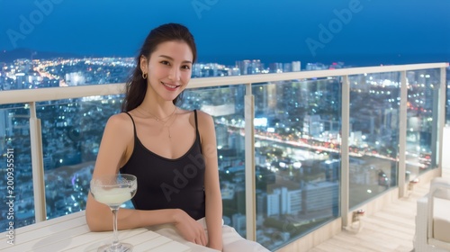Smiley Asian woman enjoying cocktails on an exclusive rooftop lounge, glass railings, modern design, and a night city horizon.
