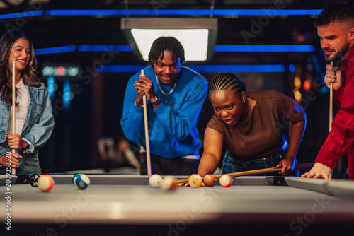 Bild auf Leinwand Diverse friends enjoying playing pool at a bar, laughing and having fun during a