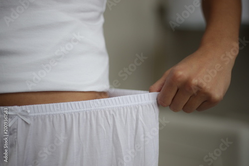 Φωτογραφία Rear view of a woman in white cotton camisole and pajama shorts standing in a modern living room, morning wellness concept