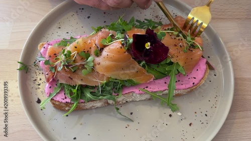 Male hands holding cutlery cutting through Smoked salmon toast with microgreens and edible flower