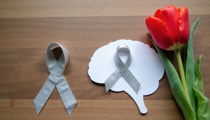 Silver awareness ribbons and brain shape with red tulip on wood table. Symbol of brain disease support hope and care for patients. Medical concept for help.