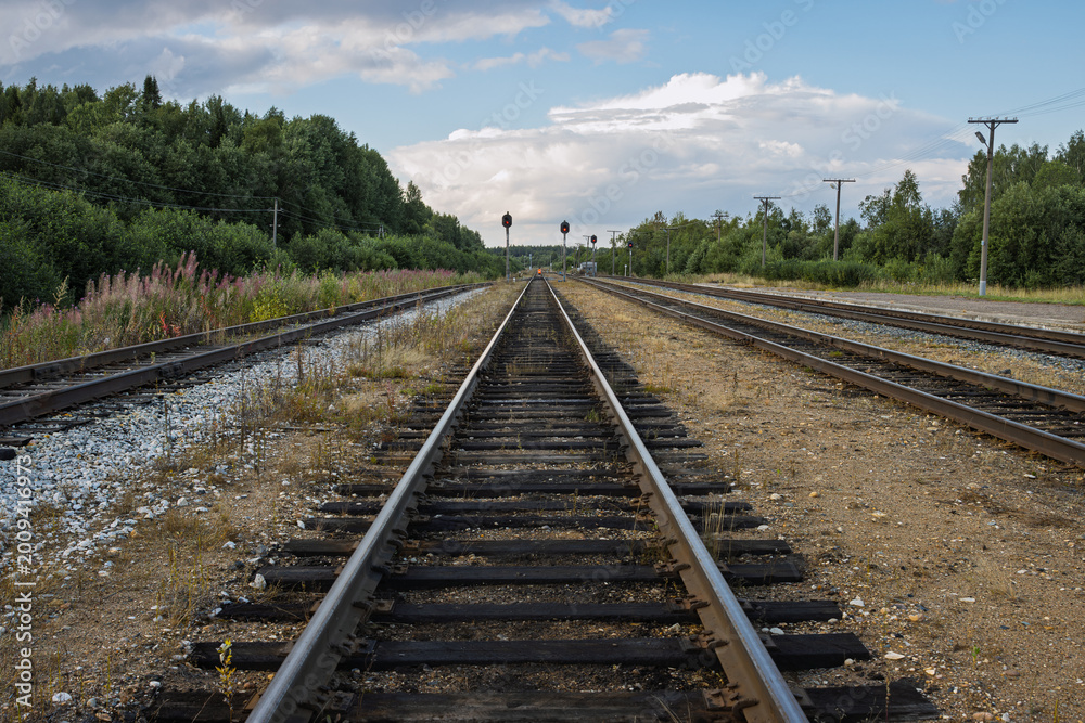 Obraz premium A deserted railway line stretches into the distance. Railroad tracks in the countryside. In the foreground are rails laid on wooden sleepers on a gravel base. In the distance are signal poles.