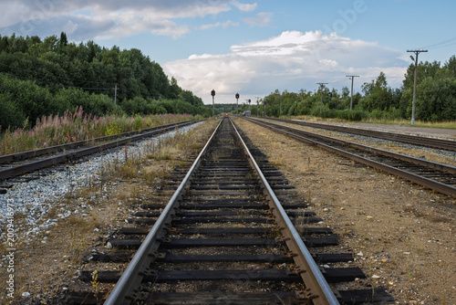 A deserted railway line stretches into the distance. Railroad tracks in the countryside. In the foreground are rails laid on wooden sleepers on a gravel base. In the distance are signal poles.