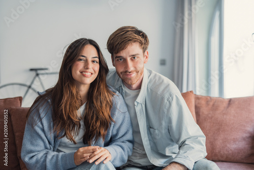 Cuadro en lienzo Smiling young couple sit close on a cozy couch in a bright living room, sharing a relaxed moment together that conveys warmth, intimacy, friendship and modern home lifestyle