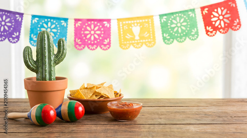 Mexican Fiesta Decoration with Tortilla Chips, Salsa, Cactus, and Maracas on a Wooden Table with Papel Picado Banners