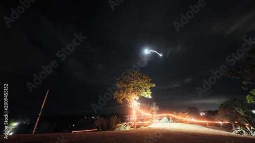 Long exposure night photography featuring light trails and a glowing tree with string lights.