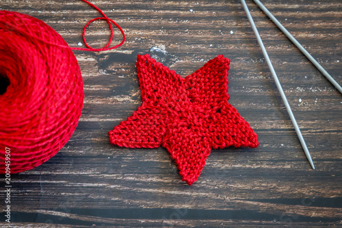Knitted red star, knitting needles, and ball of red yarn on wooden table, top view, flat lay