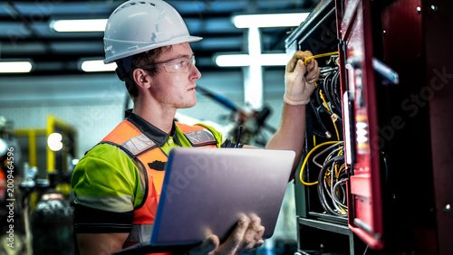 Quadro su tela A male engineer in a hard hat holds a laptop while inspecting electrical wires