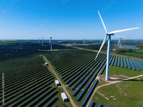 Aerial view of Chelveston Wind Farm featuring rows of solar panels and tall wind turbines under a clear blue sky in Wellingborough, England, United Kingdom.