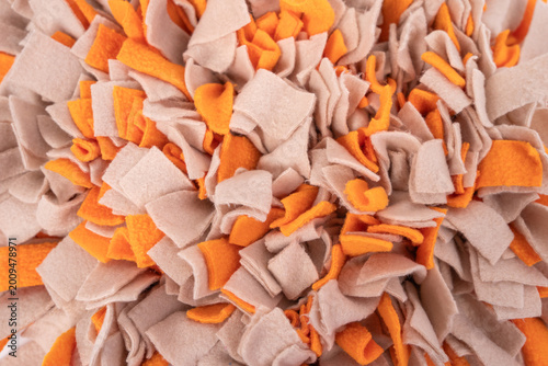 Macro close-up of handmade felt snuffle mat with dense orange and beige fabric strip, pet mental enrichment product texture background concept.