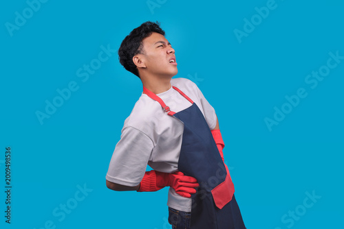 Obraz na płótnie Male Cleaner in an Apron and Rubber Gloves Holding His Lower Back in Pain with S