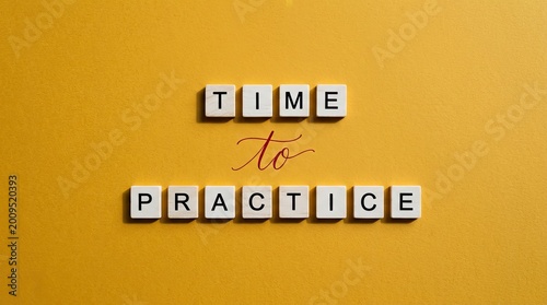 Wooden letter tiles spelling time to practice displayed against a vibrant and solid yellow background surface
