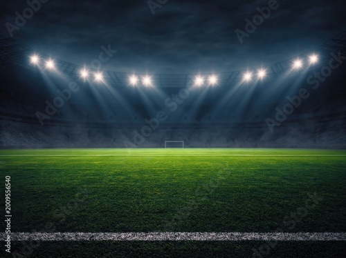 Vibrant green soccer field inside large stadium at night, brightly lit by powerful overhead floodlights creating dramatic beams of light. High quality photo