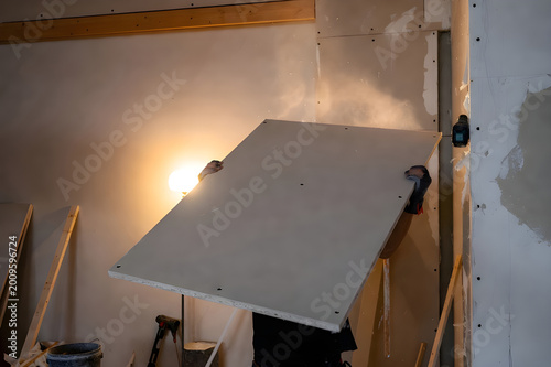 Worker Installing Drywall Sheet With Bright Work Light