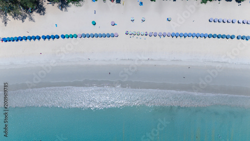 Foto Aerial view of a beach with rows of colorful umbrellas lined up near the shoreline, clear blue water, and white sand