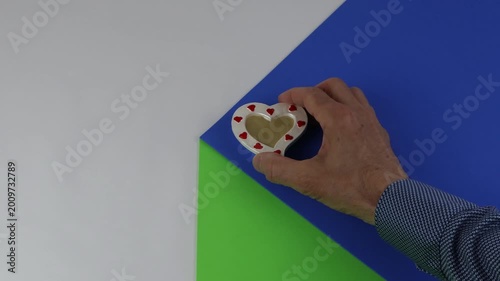 A ceramic heart placed on the edge of a table on a colored surface with a sense of copy space and chroma key