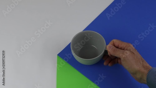 A light gray ceramic mug sits on the edge of a table on a colored surface with a sense of copy space and chroma key