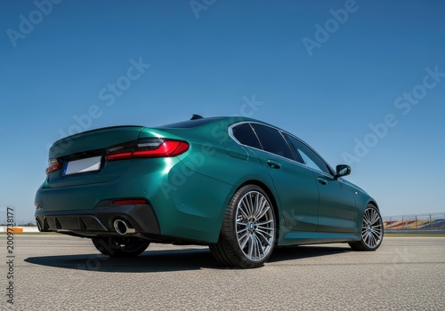 Modern green sedan sits on a race track under a clear blue sky.