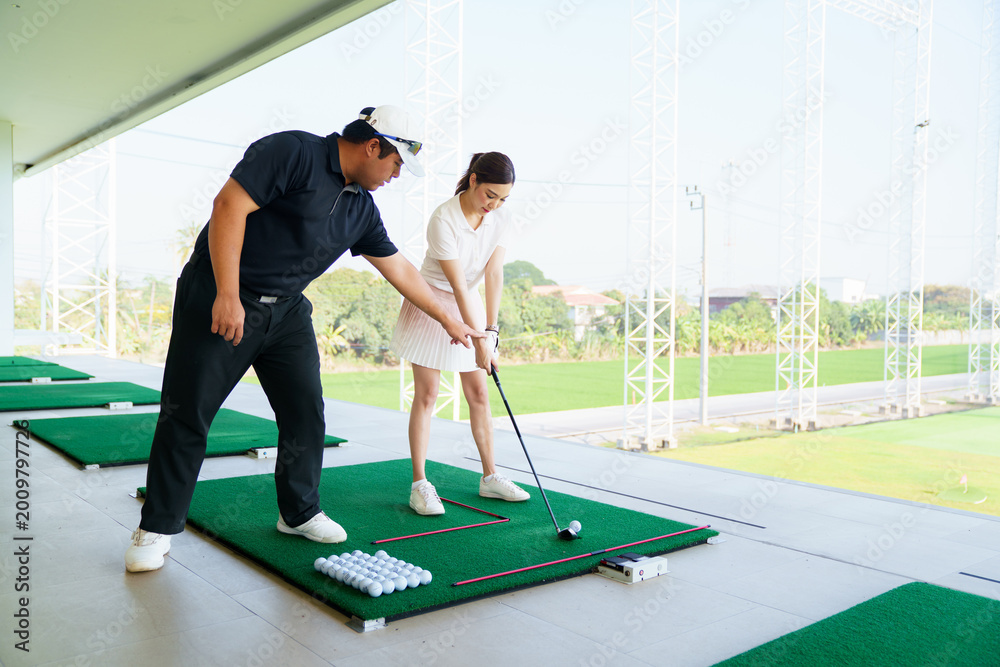 Fototapeta premium Professional golf coach adjusting posture for female student