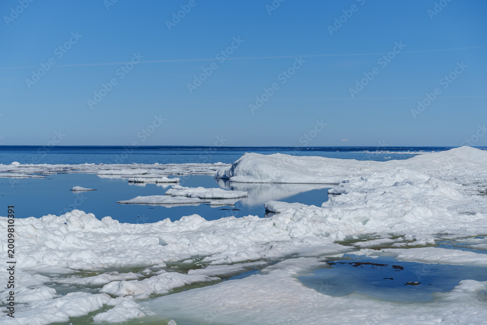 Obraz premium Arctic landscape with melting ice floes in the blue ocean under a clear sky. A beautiful polar landscape featuring chunks of melting ice and white floes drifting in the deep blue sea water.