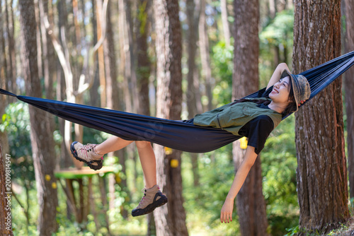 Asian woman lying on hammock between trees enjoying forest nature