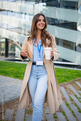Smiling woman carrying coffee and files outdoors