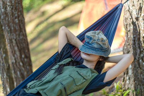 Asian woman resting on hammock with hat covering eyes in forest