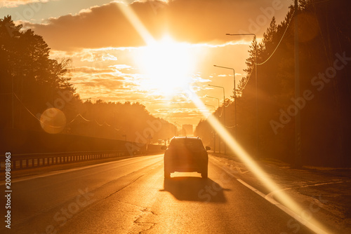 Car moving along an open highway during a vibrant golden hour, with the sun low on the horizon creating warm light and lens flare, evoking concepts of travel, freedom, and an epic road trip