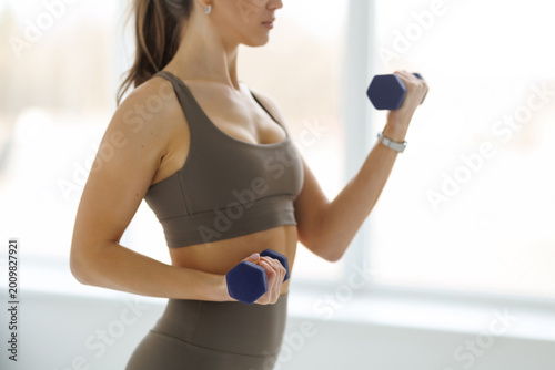 Young fit woman with dumbbells training in gym