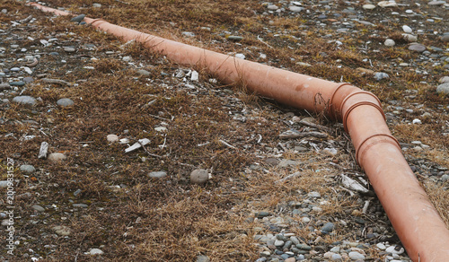 Fotografie An orange PVC pipe runs across a rugged, stony ground with dry vegetation