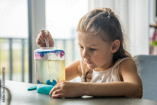 Fotografi Little girl gently making bubbles in aquarium with artemia using pipette
