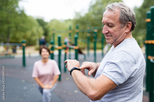 Elderly man looking at his smart bracelet in open-air sports area