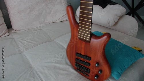 A close-up shot showing a person carefully wiping the natural wood finish of a bass guitar with a pink microfiber cloth. The strings are removed for deep cleaning and maintenance of the instrument's b