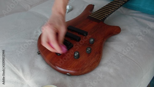 A close-up shot showing a person carefully wiping the natural wood finish of a bass guitar with a pink microfiber cloth. The strings are removed for deep cleaning and maintenance of the instrument's b