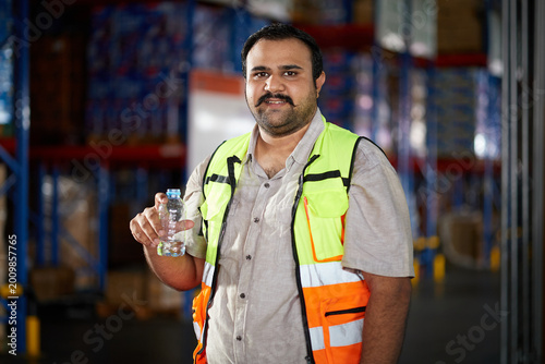 Billede på lærred Warehouse worker staying hydrated with a water bottle during a break