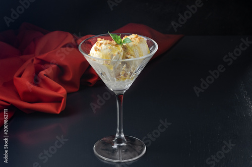 Creamy ice cream with honey and sprinkled with crunchy nuts, in a martini glass and mint on a black background.
