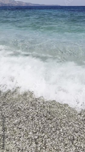 Waves crashing on pebbled beach under clear blue sky  