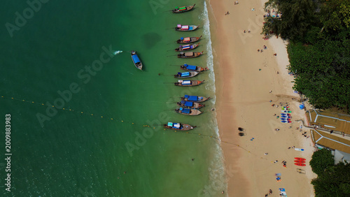 Billede på lærred Aerial view of a vibrant tropical beach, longtail boats moored in clear turquoise water, sandy shore with sunbathers, lush green coastline, idyllic vacation destination