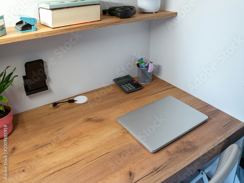 Photos A closed silver laptop sits on a light wood desk next to a calculator and pen holder