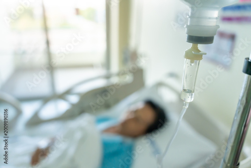 Schilderij op canvas A close-up of a saline bottle strapped to a needle pricked at the hand of a female patient lying in a hospital bed