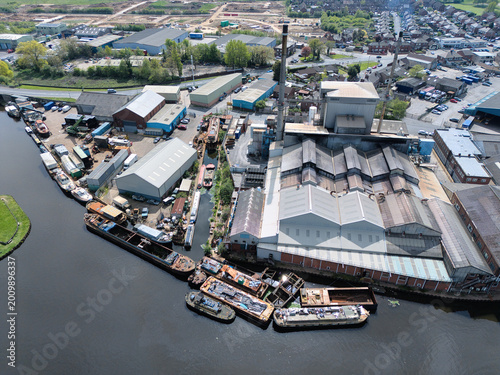 Aerial view of an industrial complex and canal with moored barges and warehouses under a clear sky in Knottingley, England, United Kingdom.